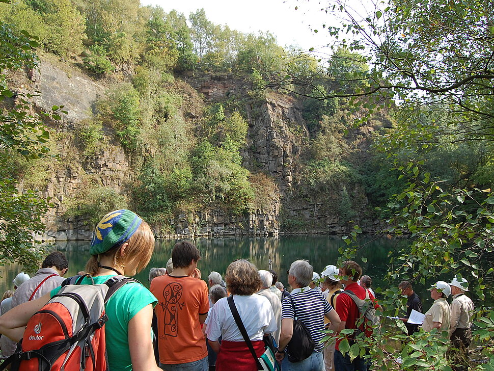 Gruppe von Exkursionsteilnehmern im Sommer vor See und Felswand