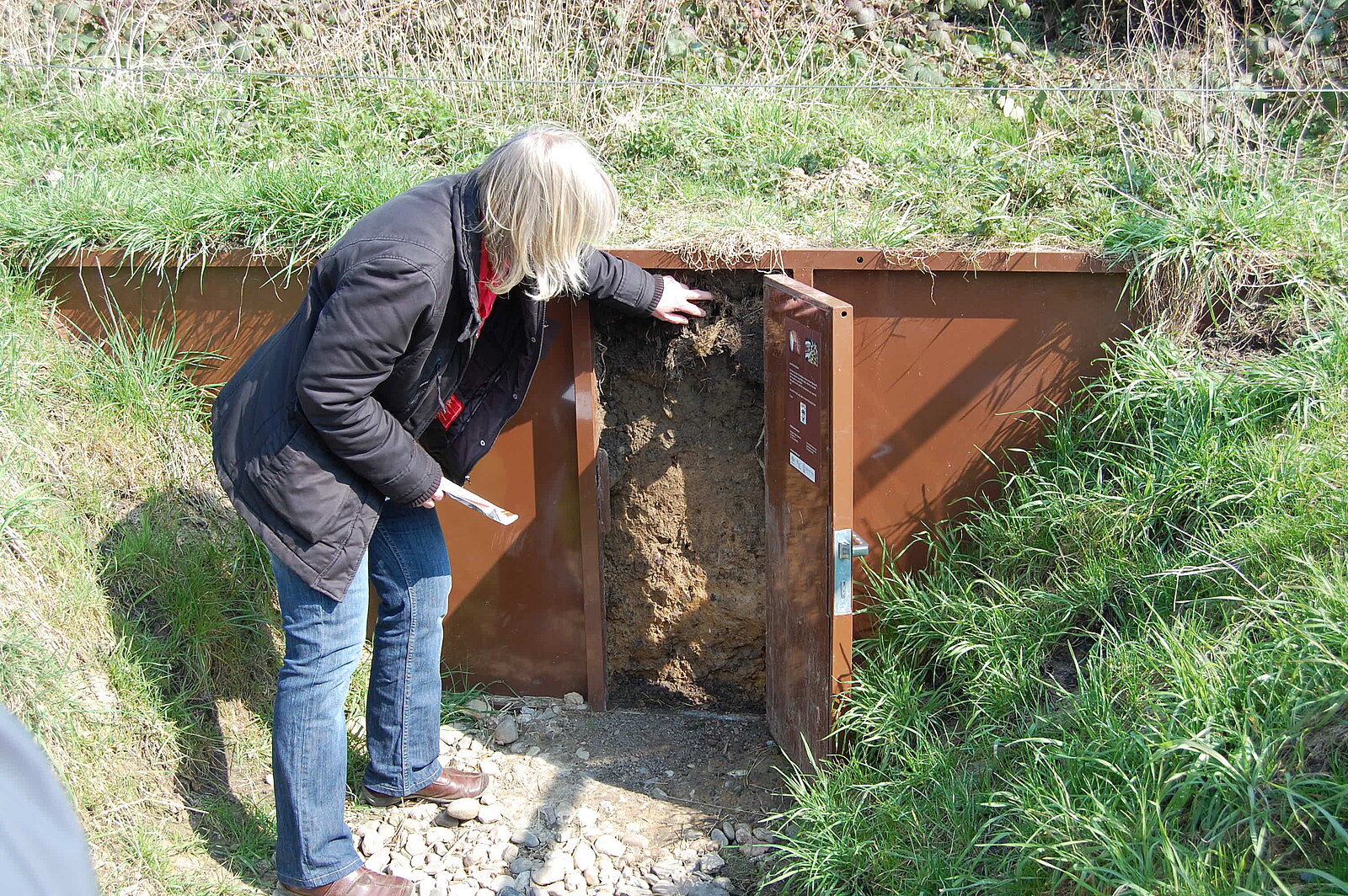 Frau öffnet Metalltür, dahinter ist der anstehende Boden zu sehen