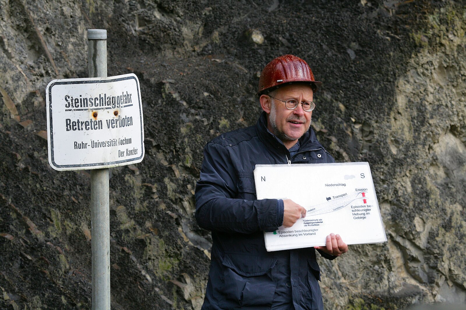 Mann mit Helm und Buch vor Felswand