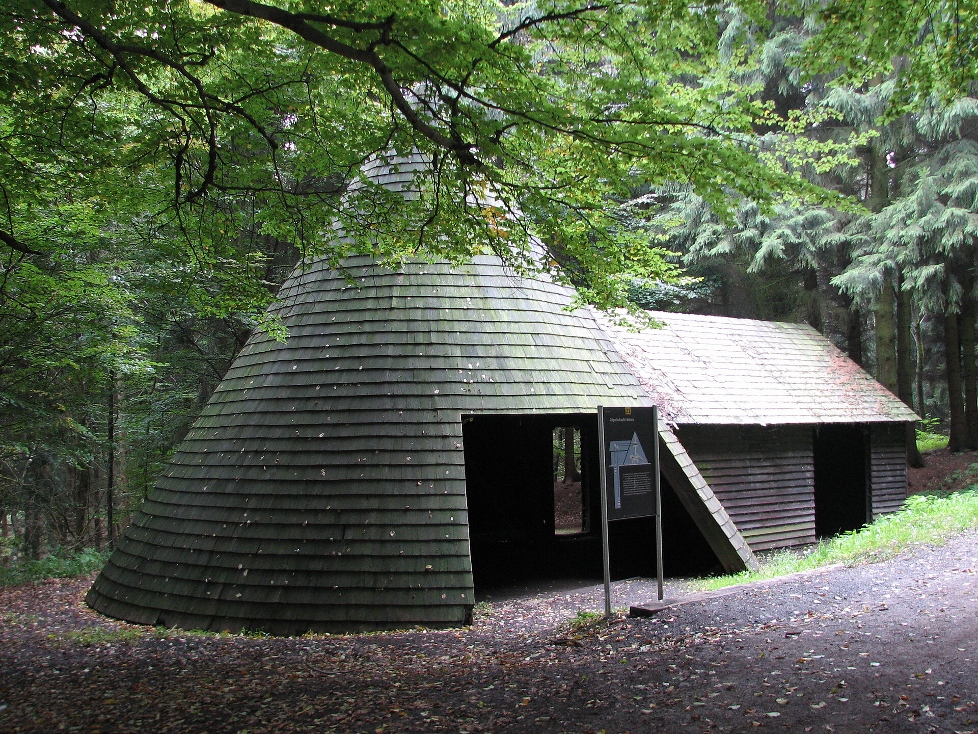 Rundes Holzgebäude mit Infotafel. 