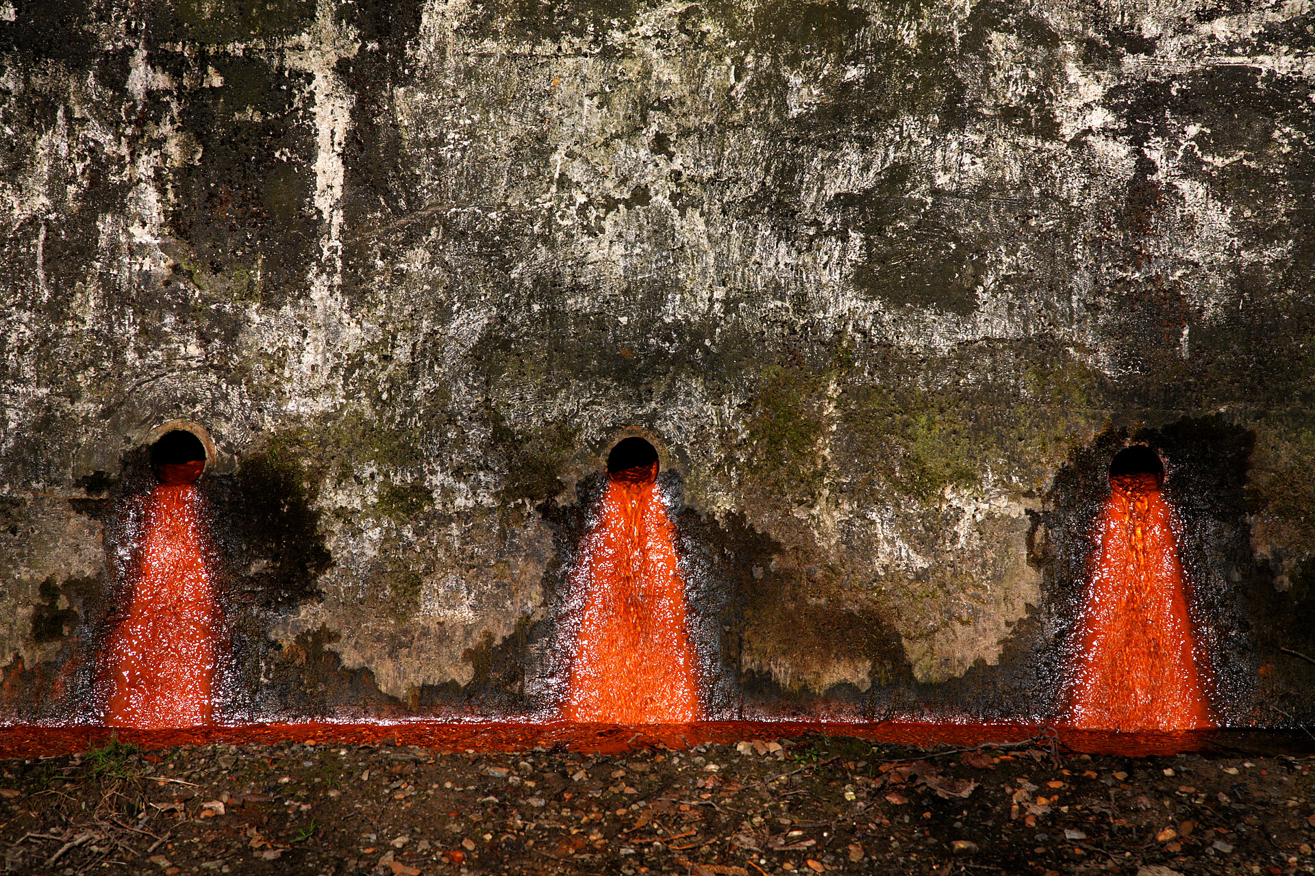 Drei Rohre aus denen rotes Wasser fließt