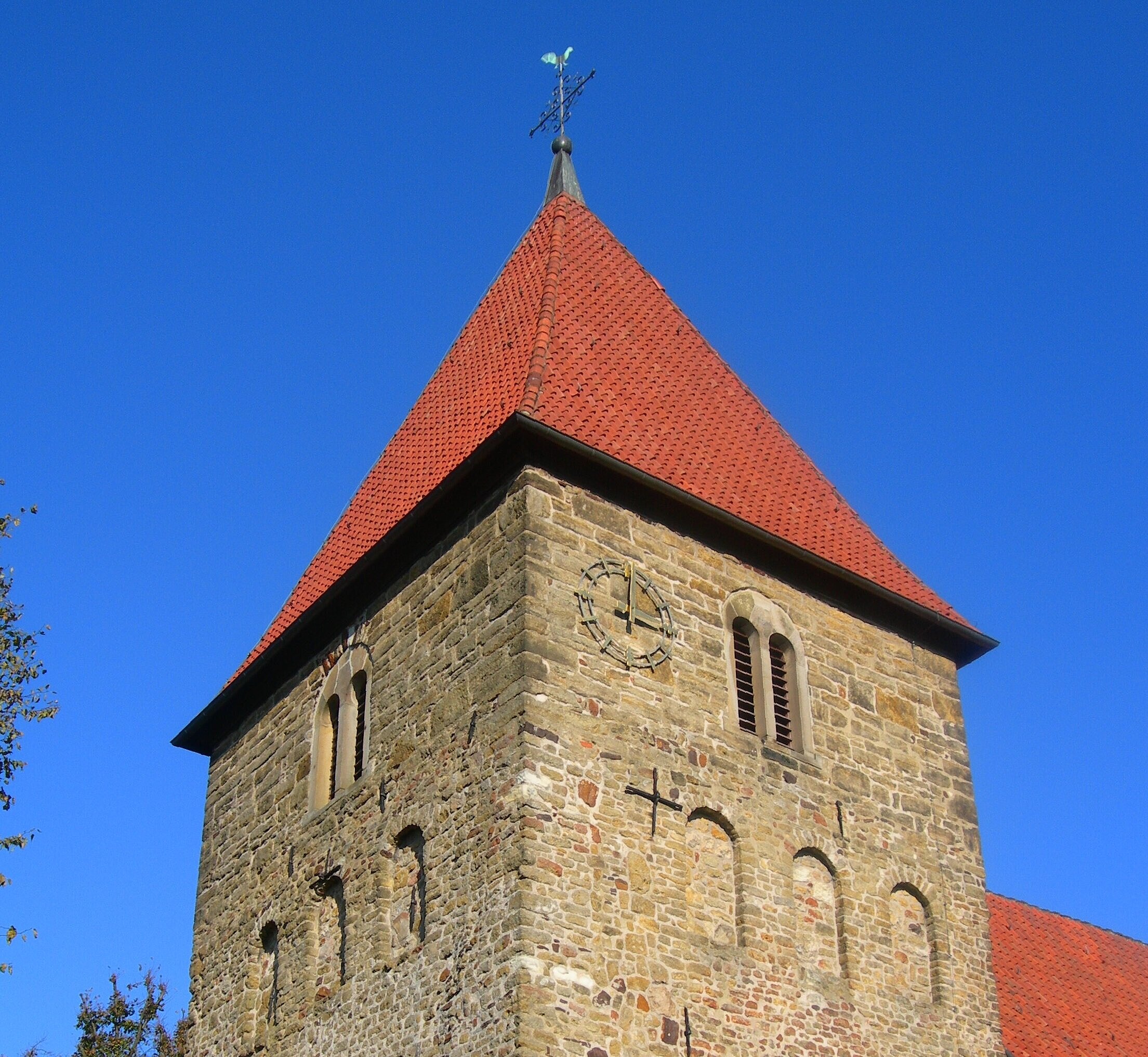 Kirchturm aus Naturstein mit rotem Ziegeldach
