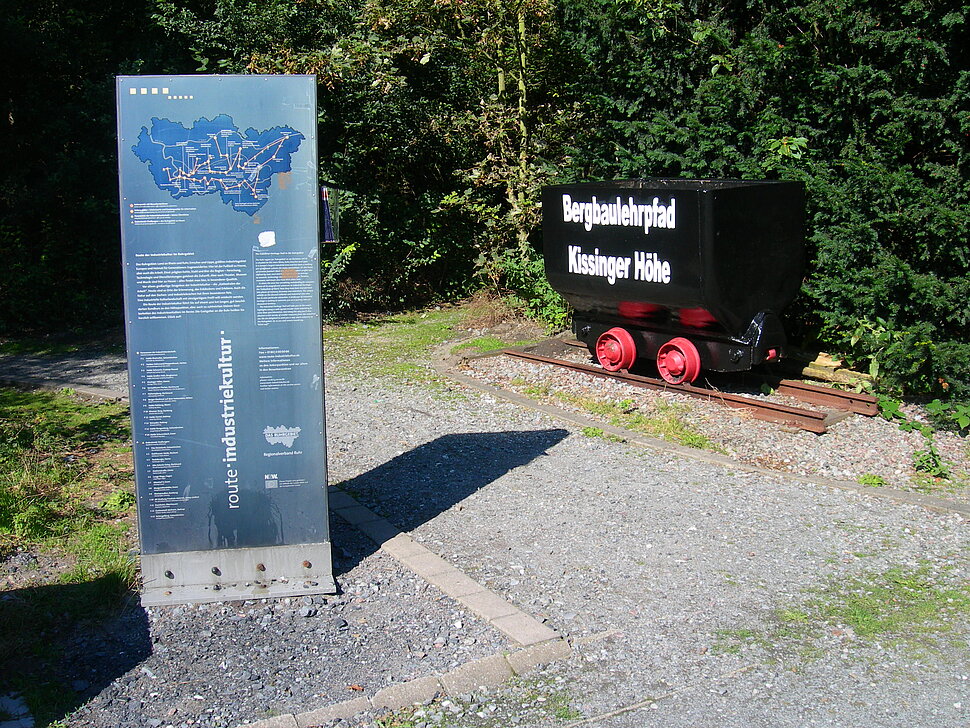 RVR-Tafel und Förderwagen mit Aufschrift "Bergbaulehrpfad Kissinger Höhe"