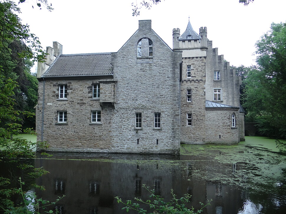 Schloss aus Naturstein hinter wassergefülltem Schlossgraben.