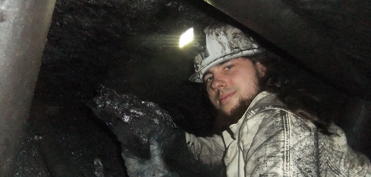 Mann mit Grubenlampe und Steinkohlebrocken in Bergwerk.
