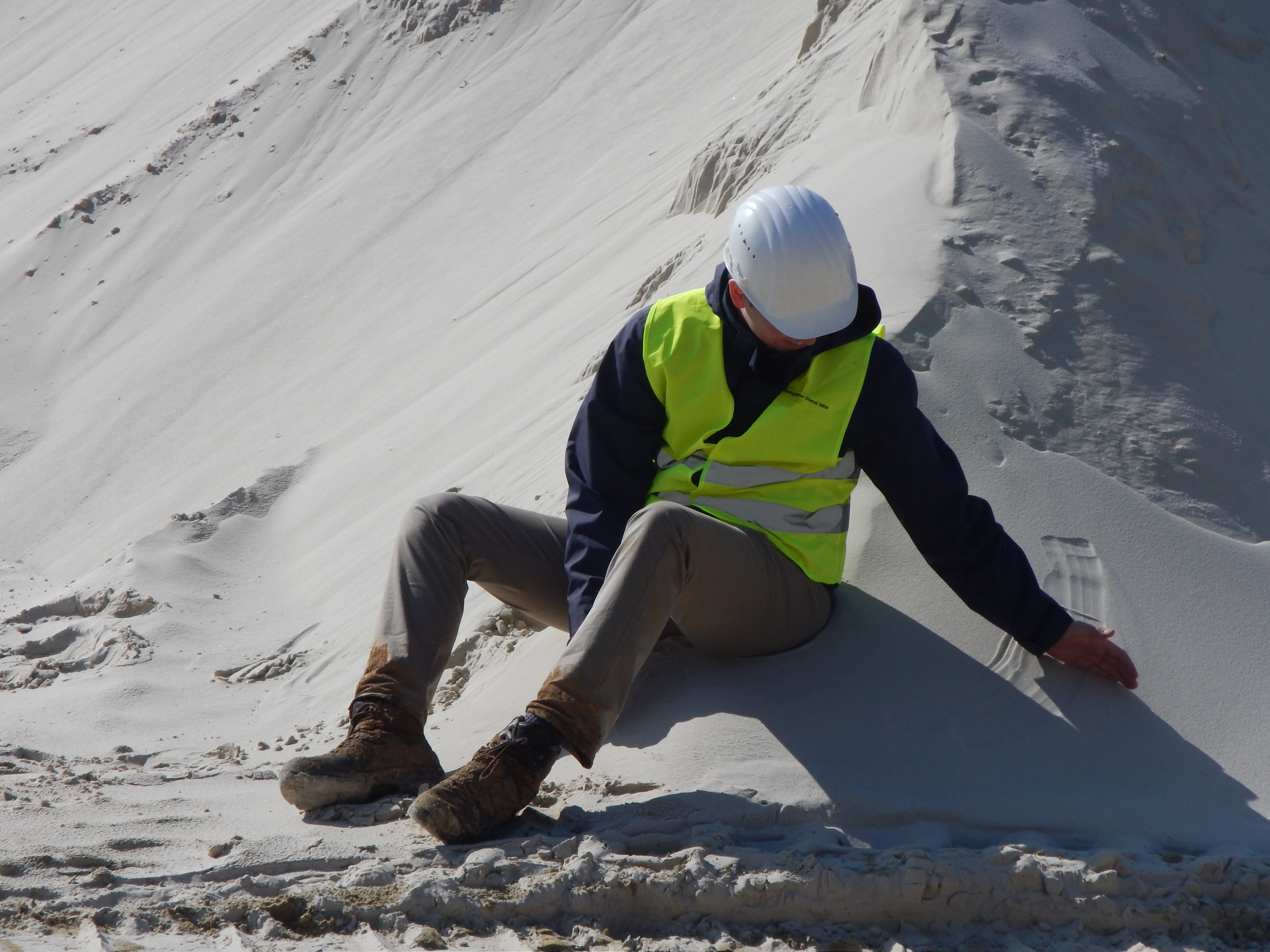 Mann mit Helm sitzt in weißem Sand