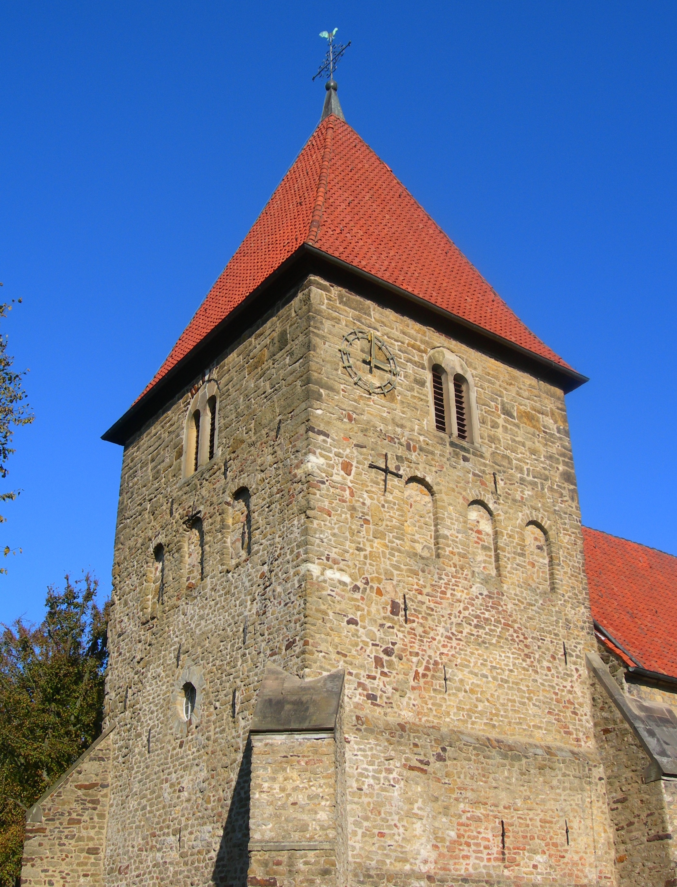 Kirchturm aus Naturstein mit rotem Ziegeldach
