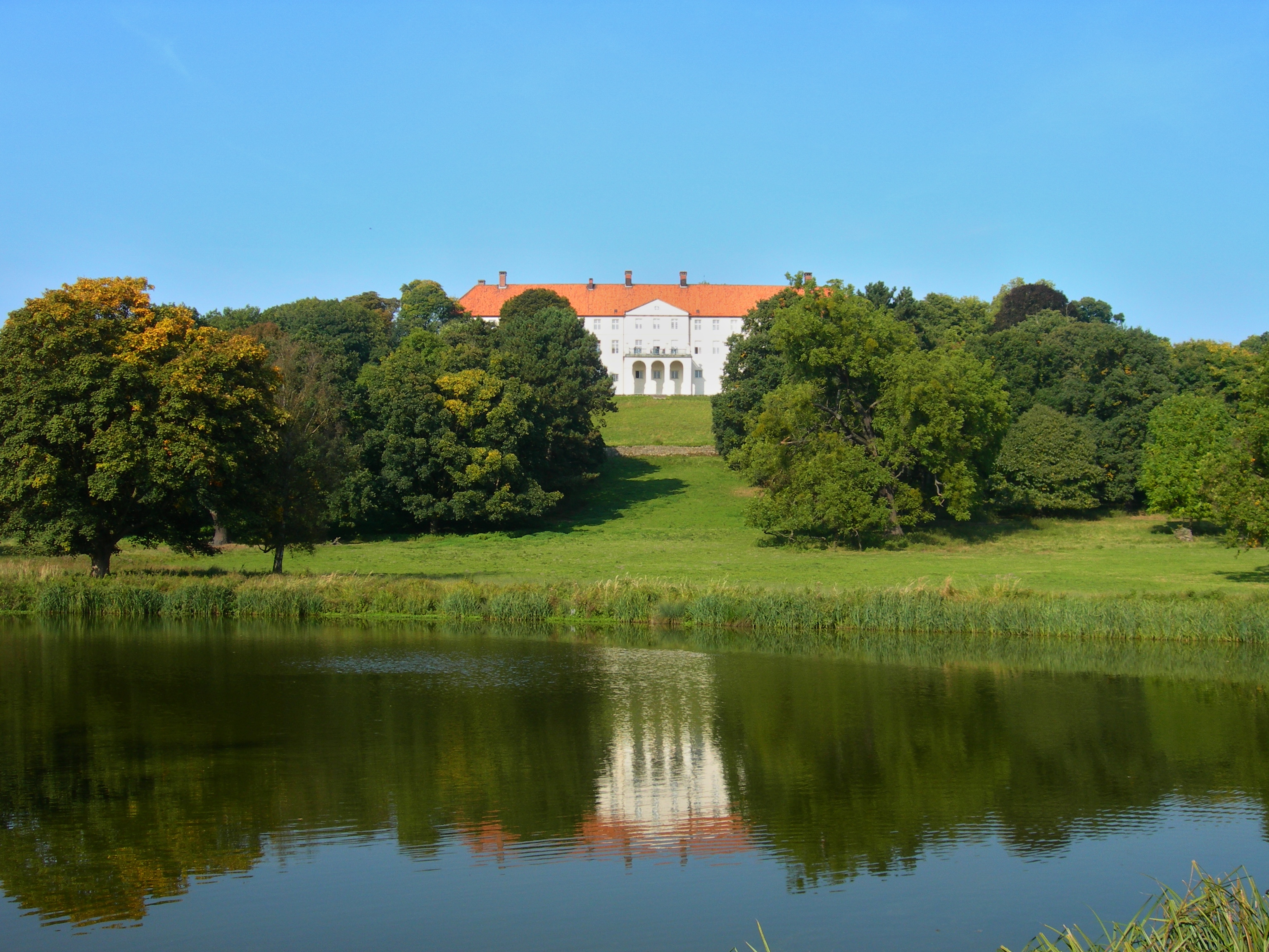 Weißes Schloss mit rotem Dach auf Anhöhe hinter See